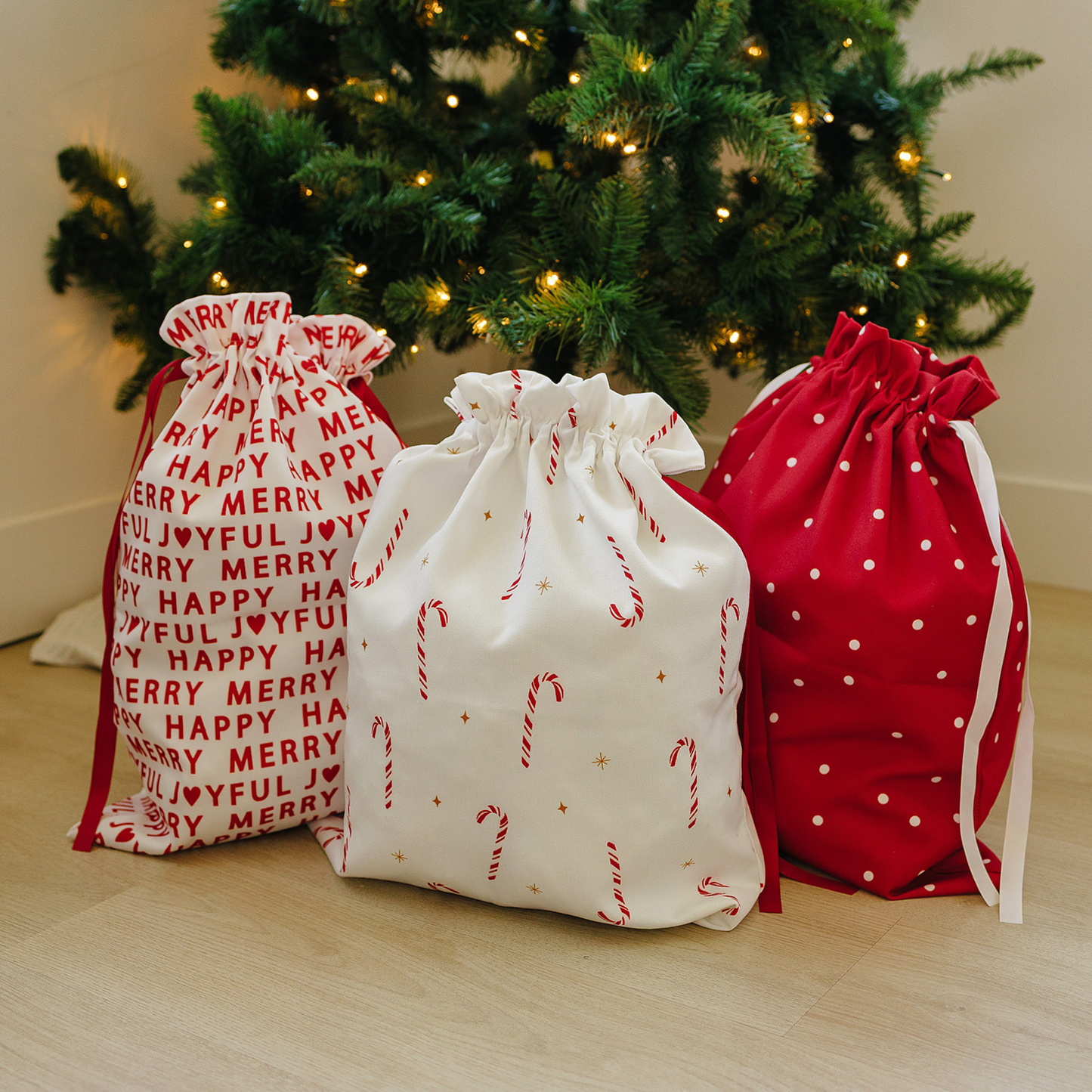 Three Christmas-themed gift bags in front of a decorated tree.