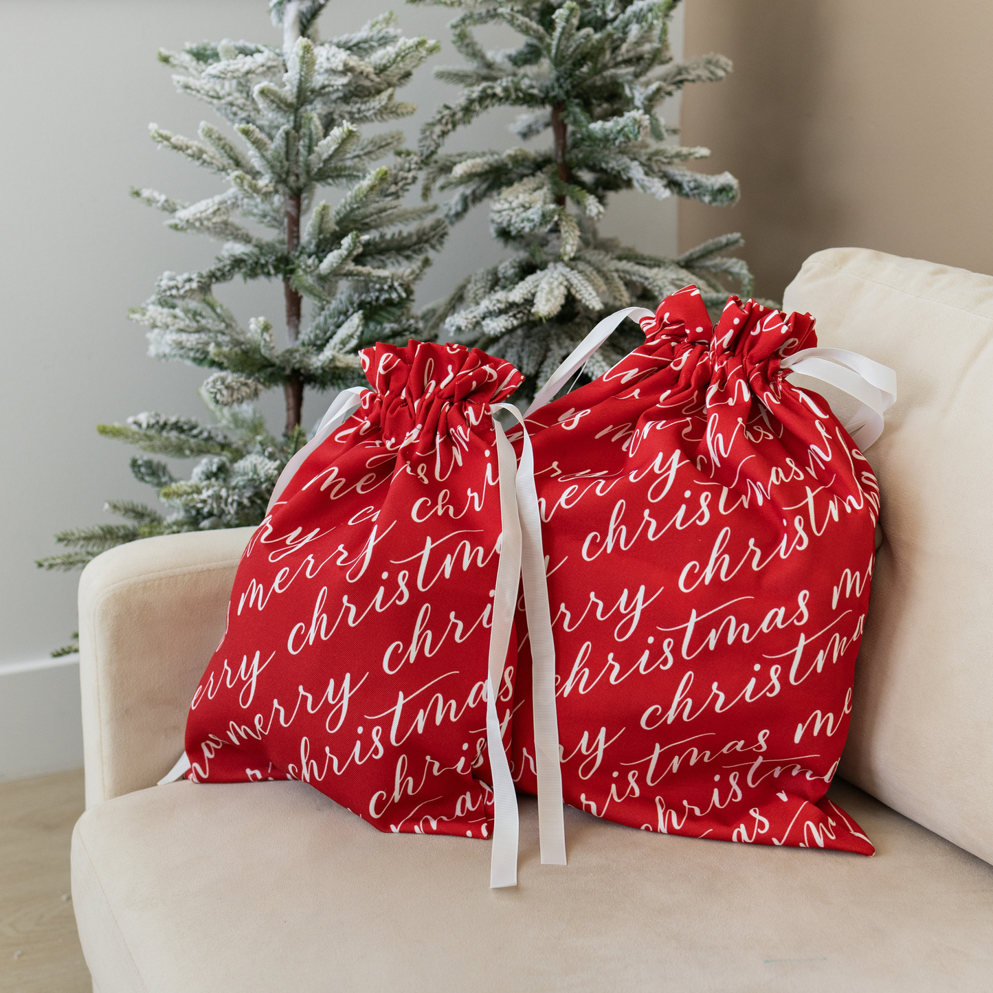 Two vibrant red fabric gift bags with 'Merry Christmas' text in white, tied with white ribbons.