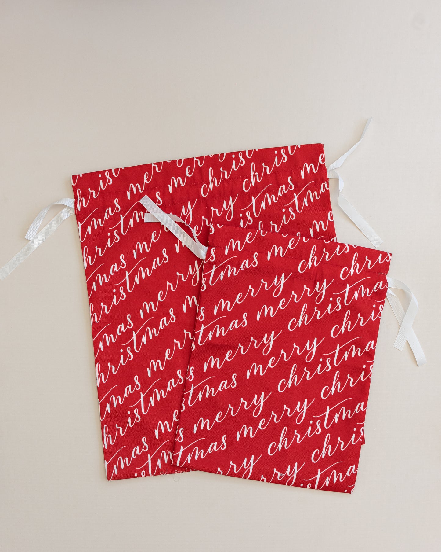 Two vibrant red fabric gift bags with 'Merry Christmas' text in white, tied with white ribbons.