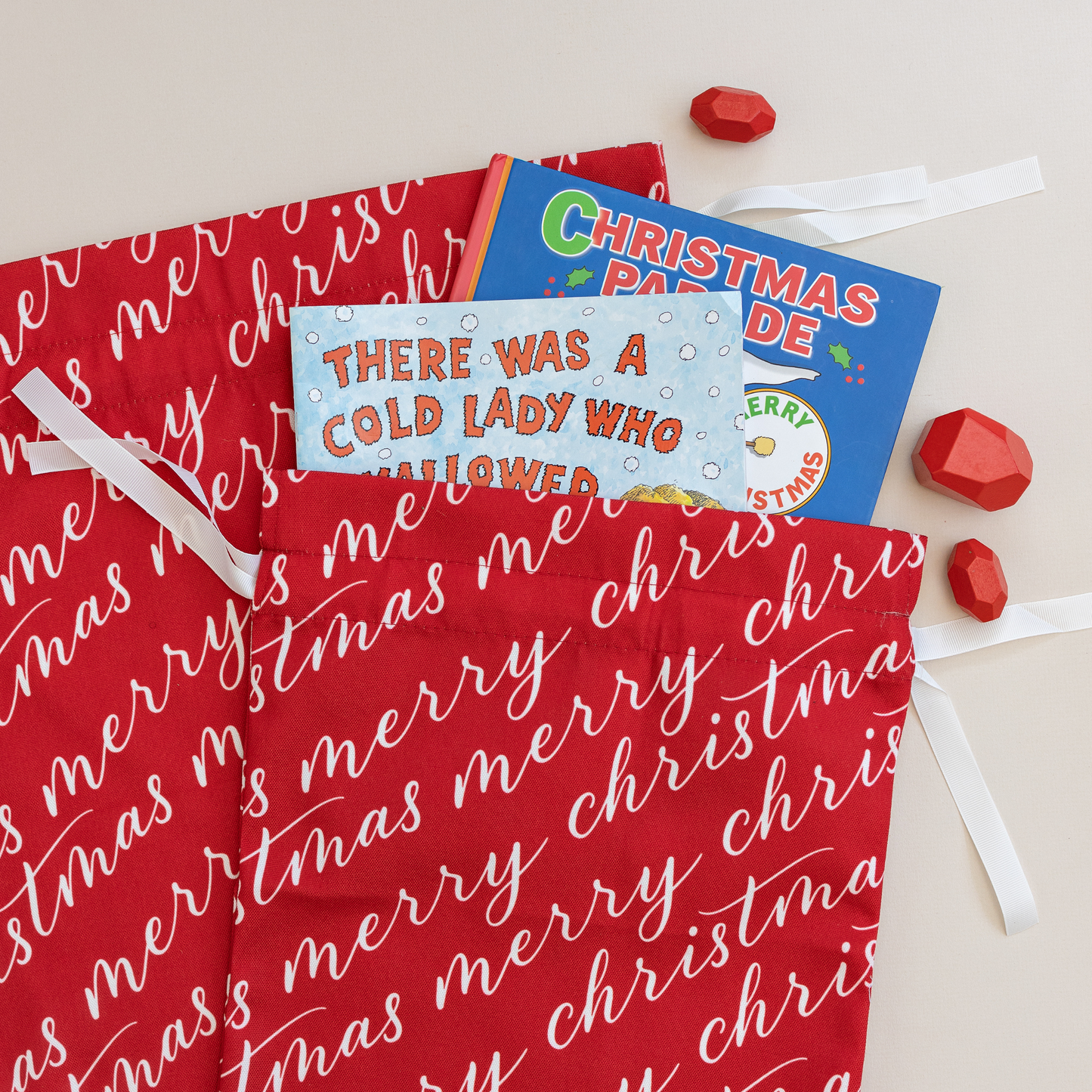 Two vibrant red fabric gift bags with 'Merry Christmas' text in white, tied with white ribbons.