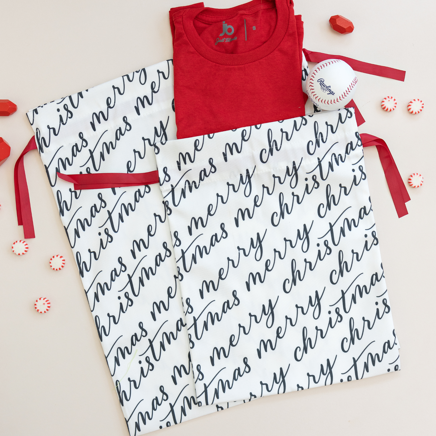 Two white fabric gift bags with 'Merry Christmas' text in black calligraphy, each adorned with a red ribbon.