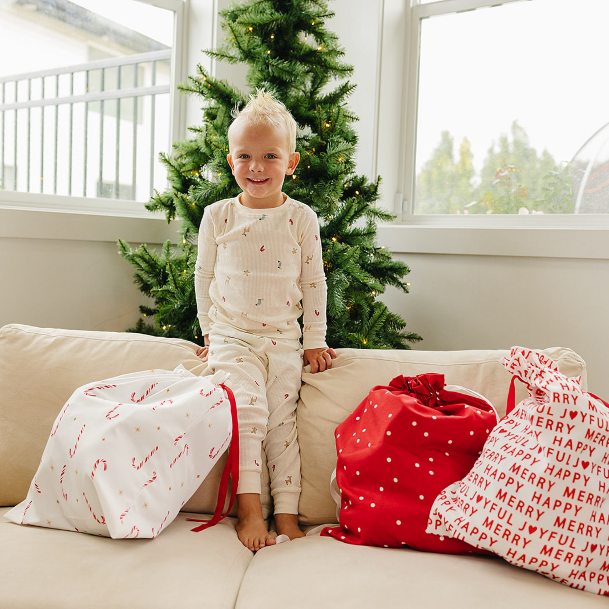 Child in pajamas sitting on a couch with Christmas presents and a decorated tree in the background