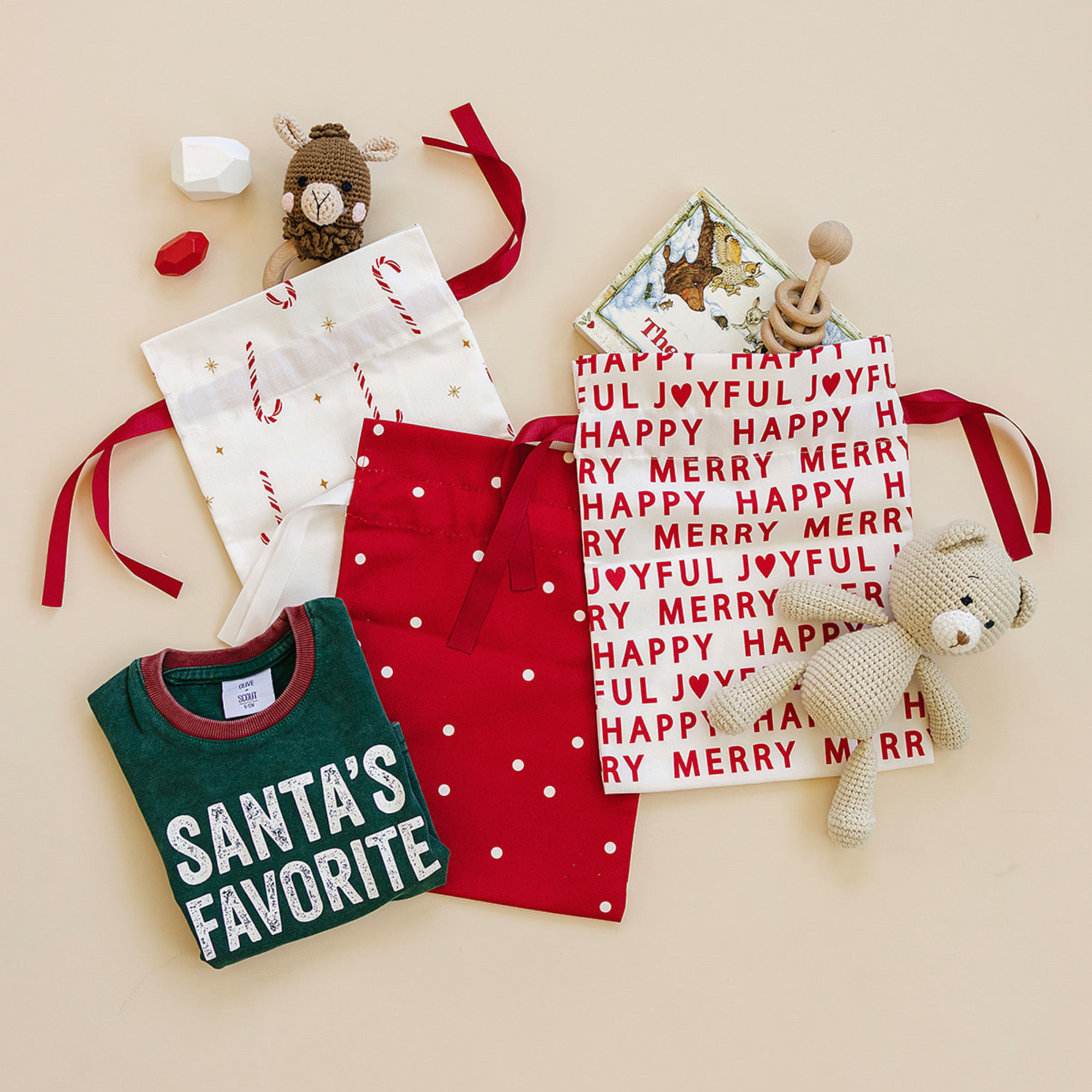Collection of Christmas-themed items including a red apron, green shirt with 'Santa's Favorite' text, and decorative cards on a beige background.