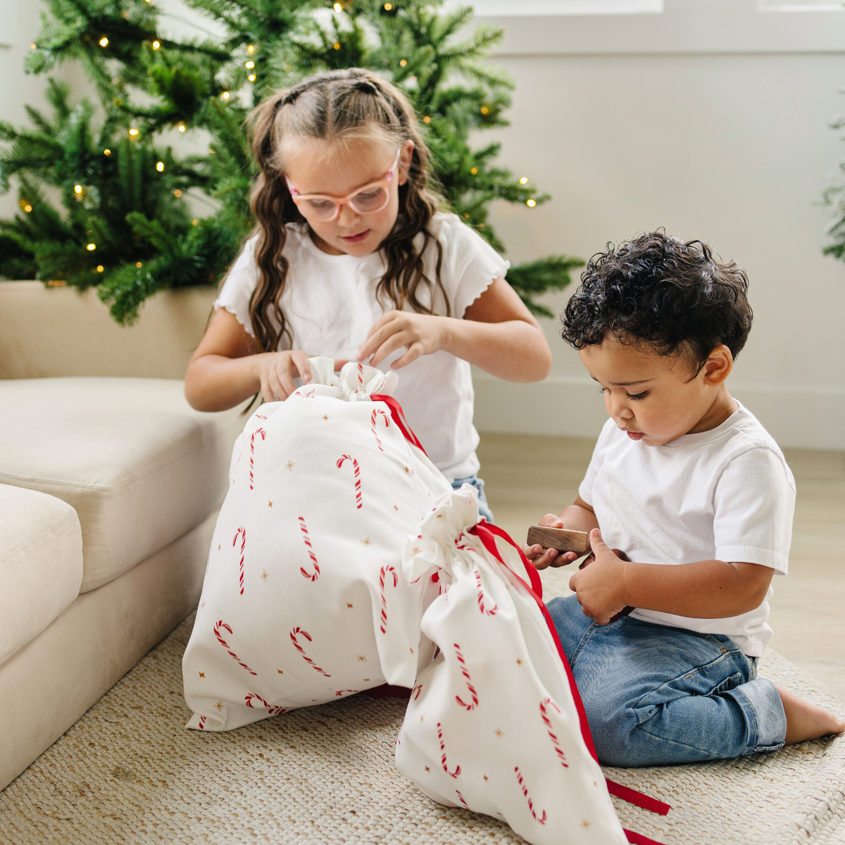 A young boy and girl opening gifts wrapped in reusable candy cane gift bags.
