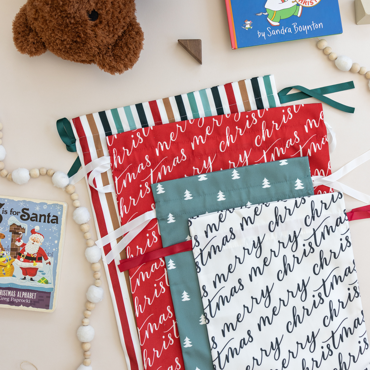 Assortment of reusable Christmas gift bags in festive holiday patterns on a light beige surface.