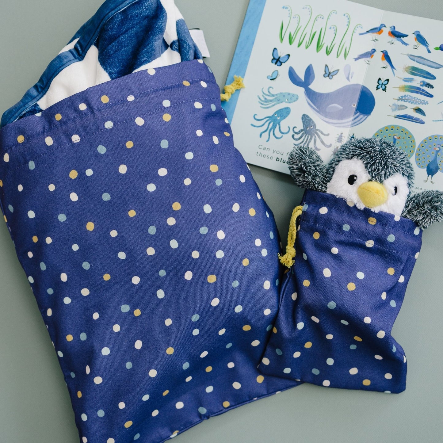 Blue polka dot bag with a penguin toy, book with marine life illustrations on a gray surface