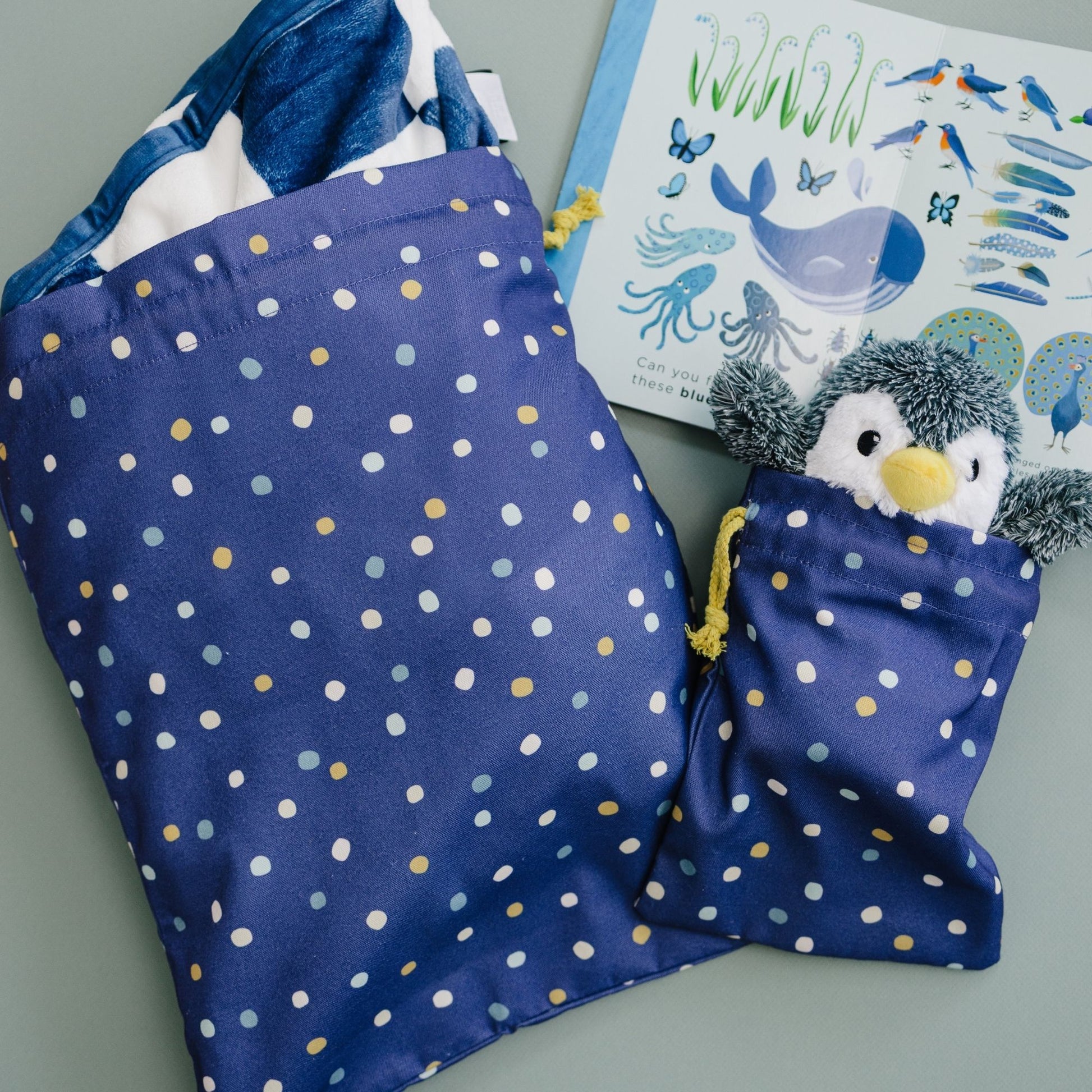 Blue polka dot bag with a penguin toy, book with marine life illustrations on a gray surface