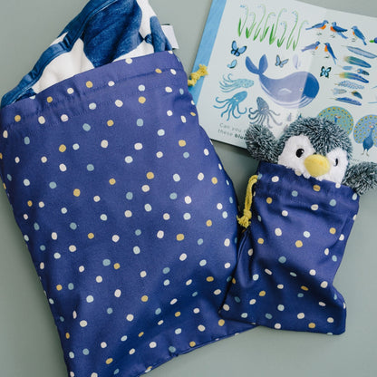 Blue polka dot bag with a penguin toy, book with marine life illustrations on a gray surface