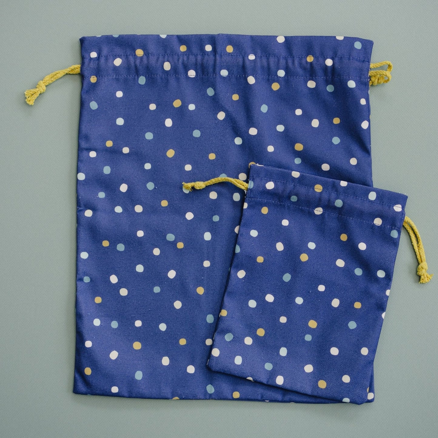 Two blue drawstring bags with white and gold polka dots on a gray background