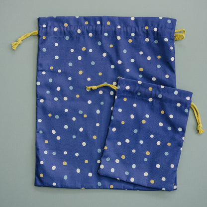 Two blue drawstring bags with white and gold polka dots on a gray background
