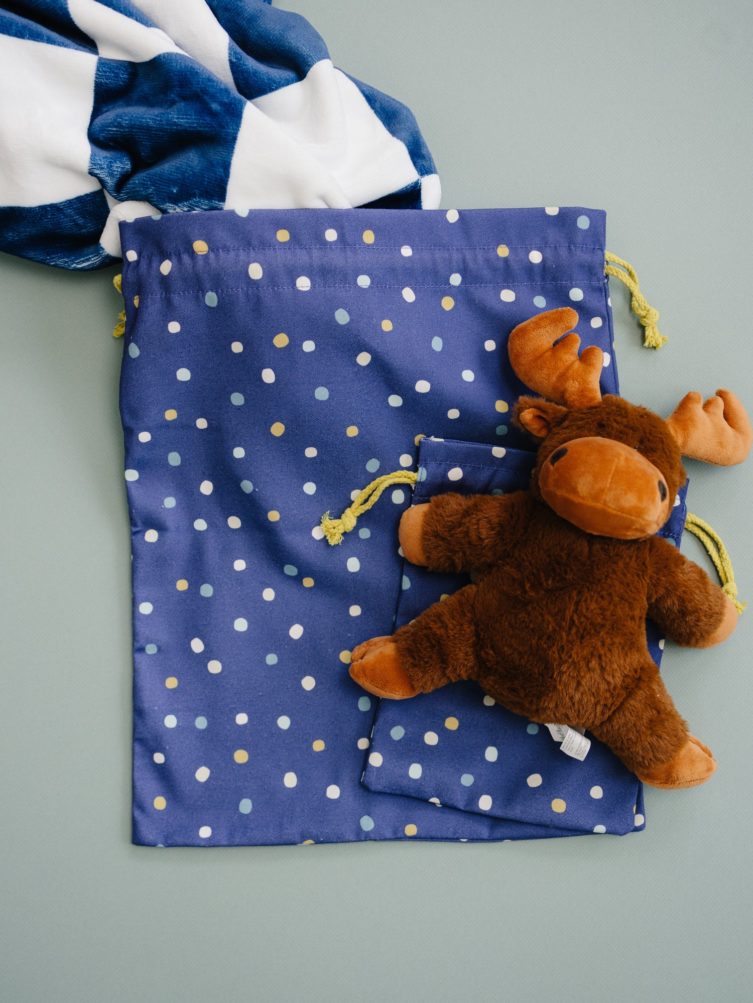 Plush moose toy on a blue drawstring bag with white polka dots against a gray background