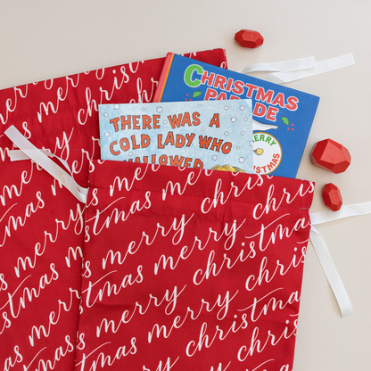 Two vibrant red fabric gift bags with 'Merry Christmas' text in white, tied with white ribbons.