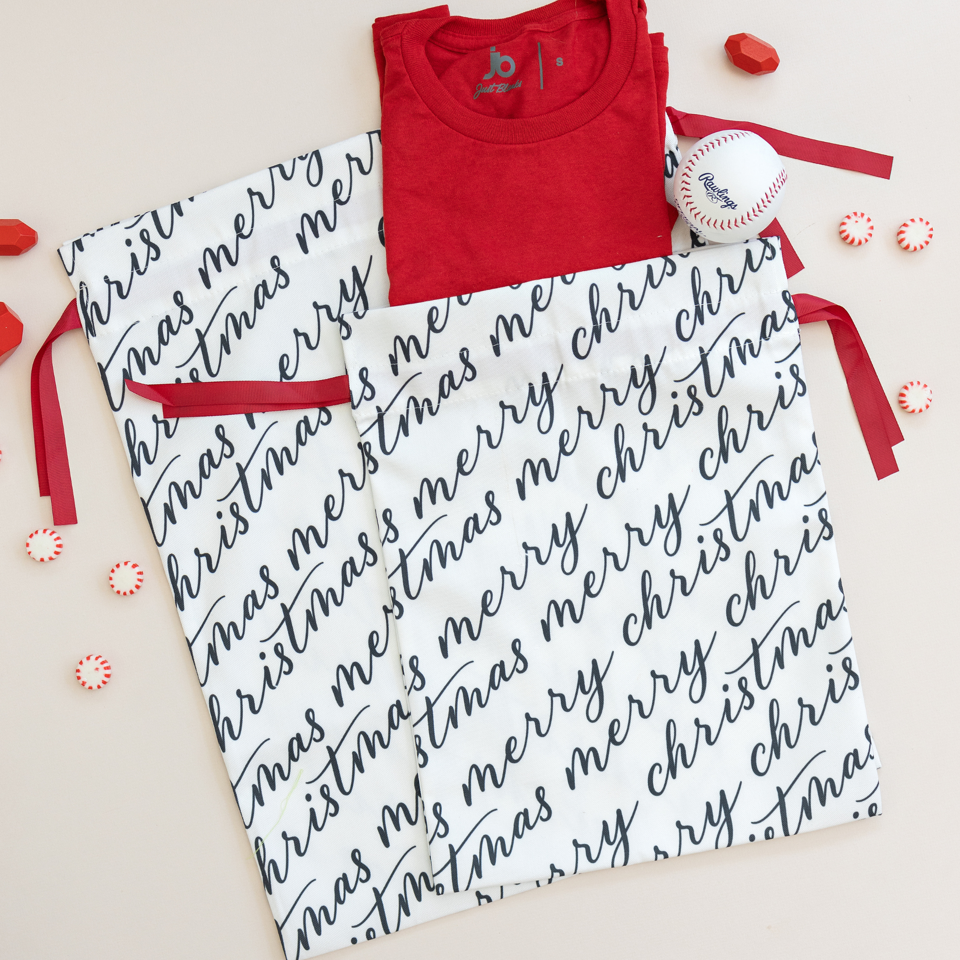 Two white fabric gift bags with 'Merry Christmas' text in black calligraphy, each adorned with a red ribbon.