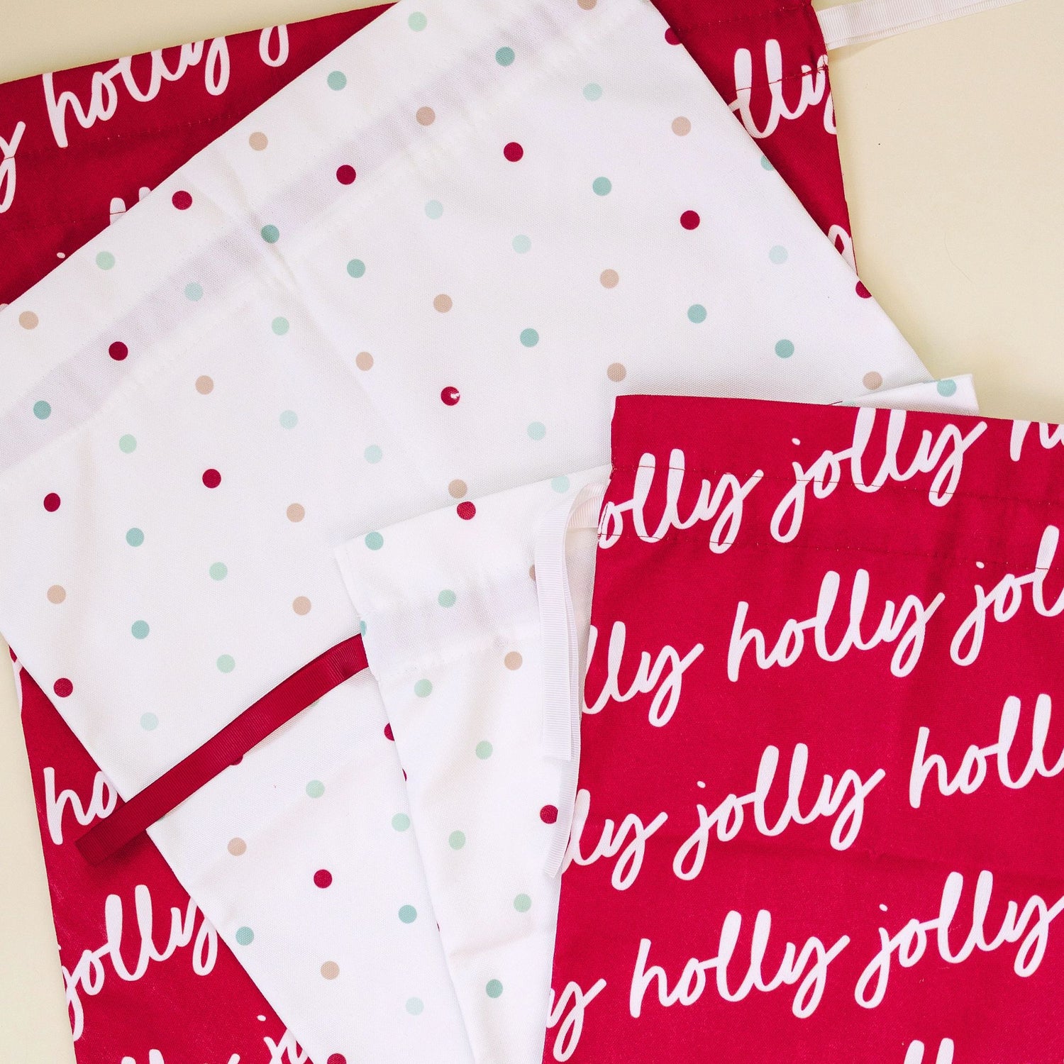 A close-up of fabric panels with a holiday theme, featuring red bags with white 'holly jolly' script and white panels with small red, mint green, and beige polka dots.
