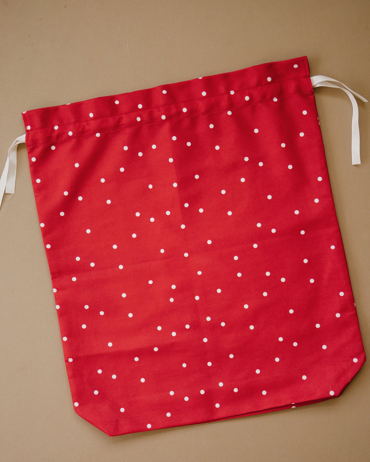 A red fabric drawstring gift bag with a white polka dot pattern, laid flat on a solid tan background.